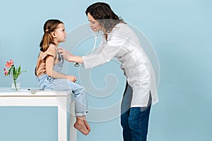 Young female doctor examining little girl with a stethoscope. Side view