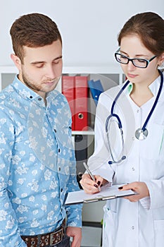 Young female doctor in glasses explaining diagnosis to her male patient. Healthcare or insurance concept.