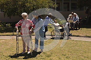 Young female doctor helping disabled senior woman in garden