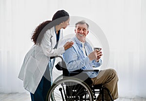 Young female doctor helping senior handicapped man in wheelchair, taking care of older patient at retirement home