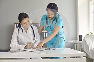 Young female doctor and her assistant working together at hospital. Physician and nurse with documents at medical office