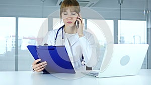 Young female doctor holding medical reports, talking on phone