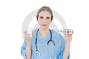 Young female doctor holding a plastic cup and medicine looking into the camera