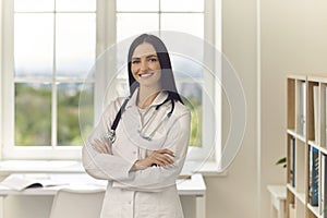 Young doctor standing arms crossed looking at camera and smiling in modern hospital office