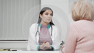 Young female doctor listening to her senior patient during medical appointment