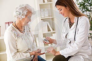 Young female doctor making diabetes blood test on senior woman