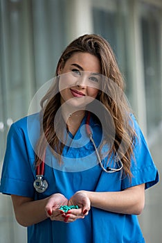 Young female doctor in in a medical equipment  holds green  pills