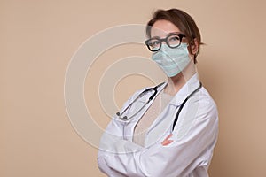 Young female doctor in medical mask and glasses looking at camera.