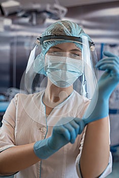 Young female doctor or nurse assistant surgeon putting on gloves standing in operation room