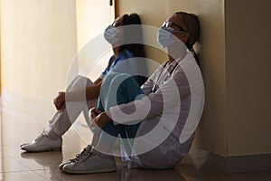 Young female doctor and nurse in medical masks sit in corridor of hospital