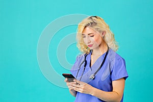 Young female doctor or nurse wearing blue scrub uniform and stethoscope using her mobile phone