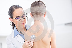 Young female doctor pediatrician examines boy patient with stethoscope