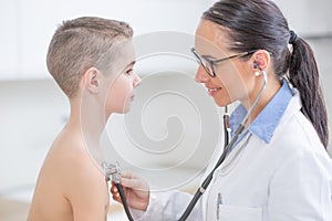 Young female doctor pediatrician examines boy patient with stethoscope