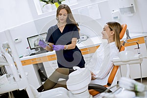 Young female doctor with protective gloves examining radiograph with her patient in the dentist office