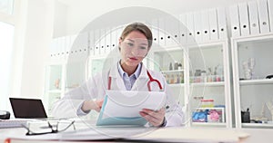 Young female doctor reviews patients medical records and test results in clinic