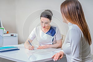 Young female doctor sits at her desk and chats to female patient while showing her test results