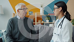 Young female doctor talking to senior patient at home expressing care and support