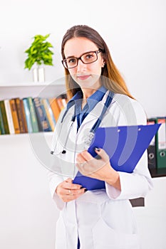 Young female doctor in uniform in doctor`s ofice with clipboard