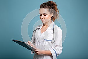 Young female doctor in uniform holding clipboard and writing