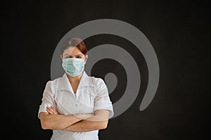 Young female doctor in uniform in a medical mask on a black background. A nurse in a department store folded her arms