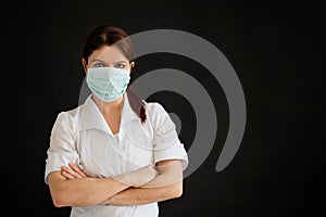 Young female doctor in uniform in a medical mask on a black background. A nurse in a department store folded her arms