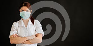 Young female doctor in uniform in a medical mask on a black background. A nurse in a department store folded her arms