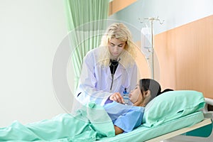 Young female doctor uses stethoscope to listen to heartbeat and lungs of recovering female patient resting in bed