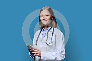 Young female doctor using smartphone, on blue studio background