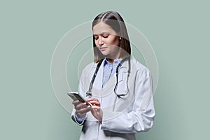 Young female doctor using smartphone, on green studio background