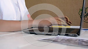 Young female doctor in a white coat working on laptop in hospital office room, therapist typing on computer consult patient online