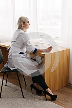 Young female doctor working desk in doctor`s room writing.