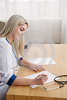 Young female doctor working desk in doctor`s room writing.