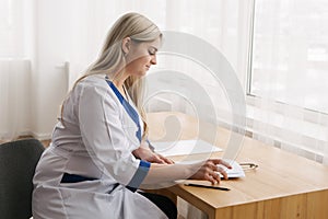 Young female doctor working desk in doctor`s room writing.