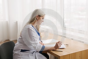 Young female doctor working desk in doctor`s room writing.