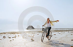 A young female dressed in light summer clothes joyfully threw up her hand while riding old vintage bicycle with a basket on the