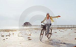 Young female dressed light summer clothes joyfully threw up her hand riding old vintage bicycle with front basket on the low tide