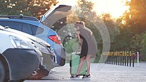 Young female driver putting luggage suitcase bag inside her car. Travelling and vacations concept