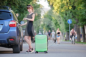 Young female driver taking out luggage suitcase bag out of her car. Travelling and vacations concept