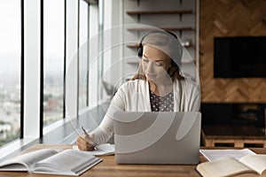 Young female in earphones have distant study course on laptop