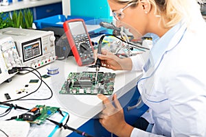 Young female electronic engineer soldering computer motherboard