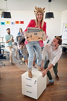 A young female employee is posing for a photo while having fun with her colleagues in the office. Employees, job, office