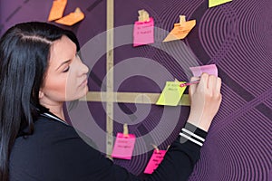 Young female employee in stylish spectacles using stickers for creation strategy of working project during brainstorming session, photo