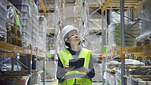 Young female employee walking on storehouse room and using tablet while working.