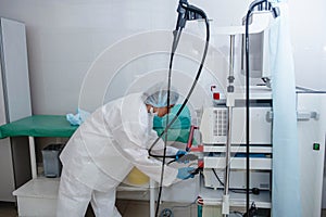 A young female endoscopist in a white protective suit, cap and gloves prepares the equipment for work.