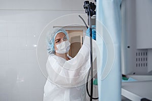A young female endoscopist in a white protective suit, cap and gloves prepares the equipment for work.