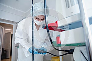 A young female endoscopist in a white protective suit, cap and gloves prepares the equipment for work.