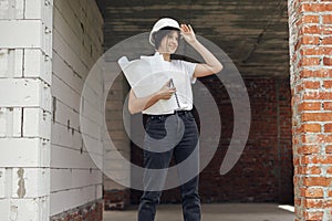 Young female engineer or construction worker in hardhat smiling against of building new modern house. Stylish happy woman