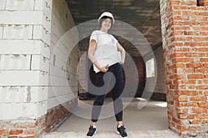 Young female engineer or construction worker in hardhat smiling against of building new modern house. Stylish happy woman