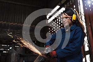 Young female engineer operating power tools with sparks in manufacturing workshop