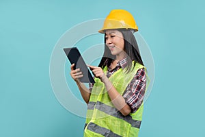 Young female engineer with a safety vest and helmet using a tablet isolated on green background